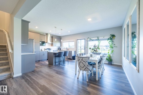 Open-concept living area featuring wood-finish flooring, a contemporary kitchen with stainless steel appliances, a kitchen island with seating, recessed lighting, and a dining area with a large window - 5403 Lark Landing Nw, Edmonton, AB - Indoor Photo Showing Dining Room