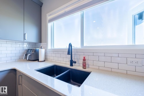 Modern kitchen with light countertops, grey cabinetry, white subway tile backsplash, and a black double basin sink with a matte black faucet - 5403 Lark Landing Nw, Edmonton, AB - Indoor Photo Showing Kitchen With Double Sink