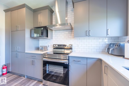Kitchen featuring grey cabinetry, white subway tile backsplash, light-toned countertops, wood-finish flooring, and stainless steel appliances including a range and range hood - 5403 Lark Landing Nw, Edmonton, AB - Indoor Photo Showing Kitchen
