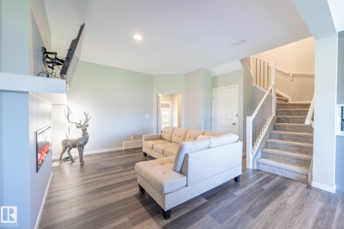 Open-concept living area featuring wood-finish flooring, recessed lighting, a built-in fireplace, and a carpeted staircase with white railings - 5403 Lark Landing Nw, Edmonton, AB - Indoor Photo Showing Living Room