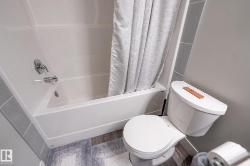 White bathtub and toilet with chrome fixtures and wood-finish flooring - 5403 Lark Landing Nw, Edmonton, AB - Indoor Photo Showing Bathroom