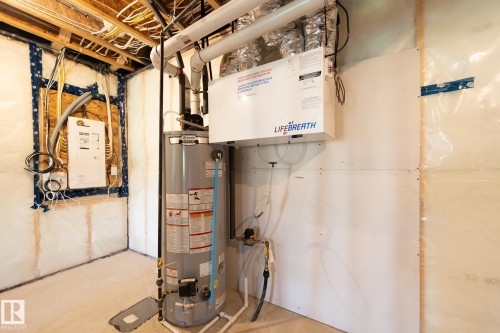 Utility area featuring a water heater, LifeBreath air exchanger, exposed ceiling joists, and electrical conduits - 5403 Lark Landing Nw, Edmonton, AB - Indoor Photo Showing Basement
