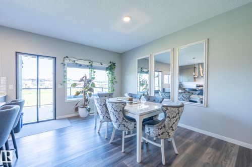 Spacious dining area featuring wood-finish flooring, a large window, and a glass-paneled patio door - 5403 Lark Landing Nw, Edmonton, AB - Indoor Photo Showing Dining Room