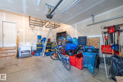 Garage featuring concrete flooring, an overhead door opener, integrated lighting, overhead storage racks, and a side access door with wood-finish steps - 5403 Lark Landing Nw, Edmonton, AB - Indoor Photo Showing Garage