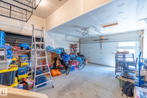 Spacious garage with a white sectional overhead door, concrete flooring, exposed ceiling joists, and overhead storage racks - 5403 Lark Landing Nw, Edmonton, AB - Indoor Photo Showing Garage
