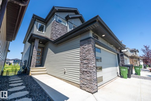 Contemporary exterior featuring horizontal siding, stacked stone accents, a modern garage door with frosted glass panels, an entry door with frosted glass inserts, and a concrete front path - 5403 Lark Landing Nw, Edmonton, AB - Outdoor