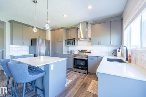 Kitchen featuring gray cabinetry, stainless steel appliances, a white subway tile backsplash, and wood-finish flooring - 5403 Lark Landing Nw, Edmonton, AB - Indoor Photo Showing Kitchen With Upgraded Kitchen