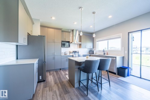 Modern kitchen featuring light gray cabinetry, stainless steel appliances, a center island with seating, a white subway tile backsplash, and wood-finish flooring - 5403 Lark Landing Nw, Edmonton, AB - Indoor Photo Showing Kitchen With Upgraded Kitchen