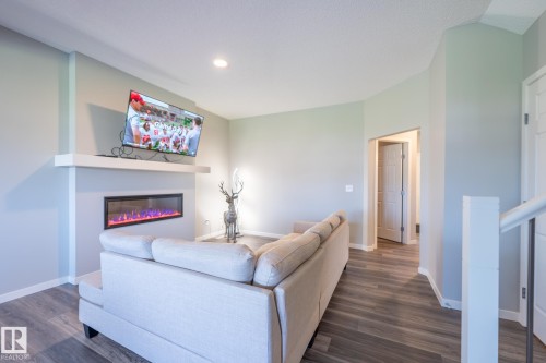 Living area featuring an electric fireplace with a floating mantel, overhead recessed lighting, and wood-finish flooring - 5403 Lark Landing Nw, Edmonton, AB - Indoor Photo Showing Living Room With Fireplace