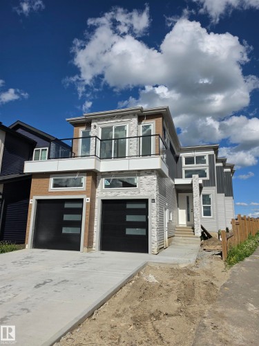 Contemporary exterior featuring a second-story balcony with glass railing, dual garage doors with frosted glass panels, mixed siding materials including stone veneer, and a concrete driveway - 231 28 Street Sw, Edmonton, AB - Outdoor With Facade