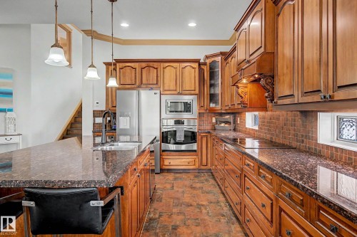Gourmet kitchen featuring extensive wood cabinetry, granite countertops, stainless steel appliances, a tile backsplash, and a large island with a double basin sink - 38 Longview Point(E), Spruce Grove, AB - Indoor Photo Showing Kitchen With Double Sink With Upgraded Kitchen