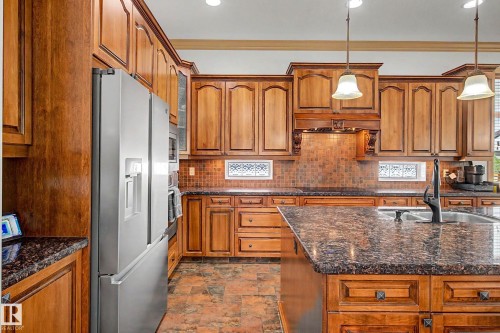 Kitchen featuring wood cabinetry, dark speckled countertops, stainless steel refrigerator, island with sink, and pendant lighting - 38 Longview Point(E), Spruce Grove, AB - Indoor Photo Showing Kitchen With Double Sink