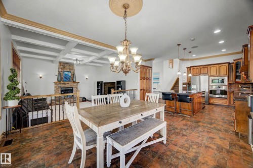 Open-concept living space featuring wood-finish flooring, a coffered ceiling, a stone fireplace, wood cabinetry, and a kitchen island with pendant lighting - 38 Longview Point(E), Spruce Grove, AB - Indoor Photo Showing Dining Room