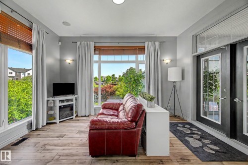 Spacious room featuring wood-finish flooring, large windows with horizontal blinds, and a built-in electric fireplace - 38 Longview Point(E), Spruce Grove, AB - Indoor Photo Showing Other Room