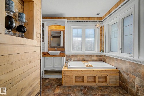 Spacious bathroom featuring a built-in soaking tub with a wood-finish surround, multiple large windows, and a crystalline chandelier - 38 Longview Point(E), Spruce Grove, AB - Indoor Photo Showing Bathroom