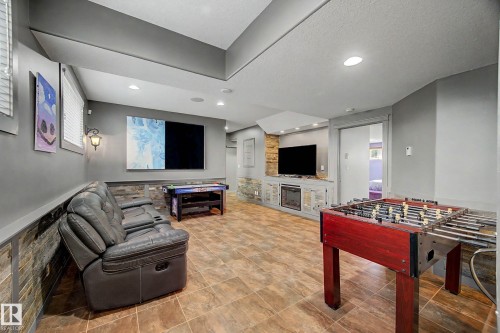 Spacious recreation room featuring tile flooring, a built-in media console with an electric fireplace, recessed lighting, and a stone accent wall - 38 Longview Point(E), Spruce Grove, AB - Indoor