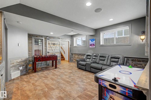 Finished lower level featuring recessed lighting, tile flooring, two windows with blinds, a wood-paneled accent wall, and barn doors - 38 Longview Point(E), Spruce Grove, AB - Indoor