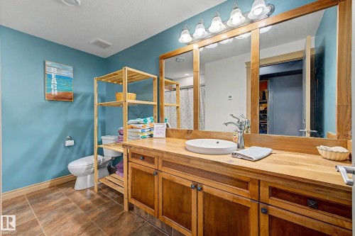 Bathroom featuring a wood-finish vanity with an oval vessel sink and a wall-mounted light fixture above a large mirror - 38 Longview Point(E), Spruce Grove, AB - Indoor Photo Showing Bathroom