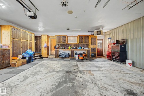 Spacious garage featuring extensive built-in wooden cabinetry, a dedicated workbench area, corrugated metal wall paneling, and a checkerboard pattern floor section - 38 Longview Point(E), Spruce Grove, AB - Indoor Photo Showing Garage