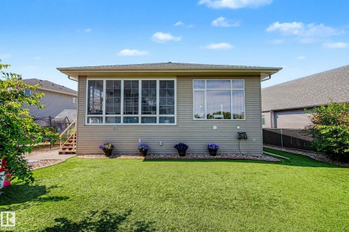 Expansive rear exterior featuring a sunroom addition with large windows, tan siding, and a well-maintained green lawn - 38 Longview Point(E), Spruce Grove, AB - Outdoor