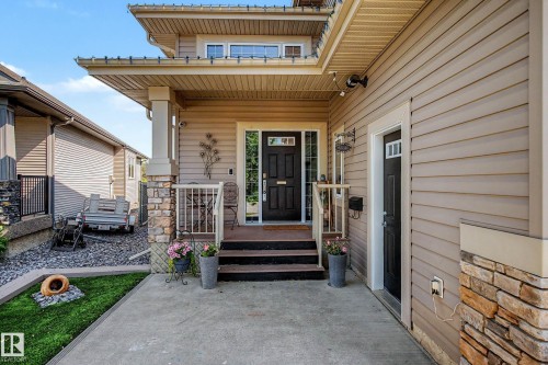 Inviting front entrance featuring a dark wood-finish door with sidelights, a covered porch with stone-clad columns, and a concrete walkway - 38 Longview Point(E), Spruce Grove, AB - Outdoor With Deck Patio Veranda