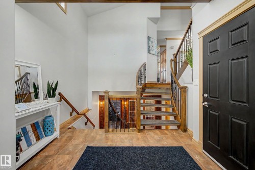 Entry foyer with a black paneled door and light wood trim, featuring a multi-level staircase with wood treads and wrought iron balusters - 38 Longview Point(E), Spruce Grove, AB - Indoor Photo Showing Other Room