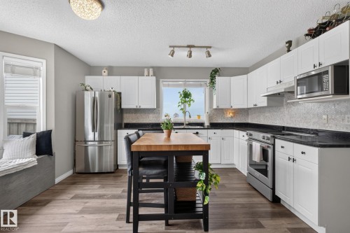 Contemporary kitchen featuring white cabinetry, dark countertops, and stainless steel appliances - 833 Mcallister Crescent Sw, Edmonton, AB - Indoor Photo Showing Kitchen With Double Sink