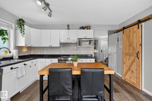 Well-appointed kitchen featuring white cabinetry, black countertops, and a full tile backsplash - 833 Mcallister Crescent Sw, Edmonton, AB - Indoor Photo Showing Kitchen With Double Sink