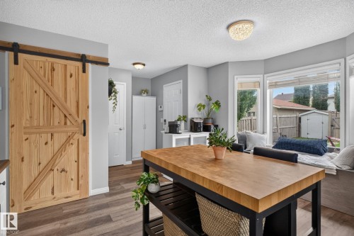 Kitchen area featuring a butcher block island with open shelving, wood-finish flooring, a natural wood barn door, and a bay window with an integrated bench seat - 833 Mcallister Crescent Sw, Edmonton, AB - Indoor