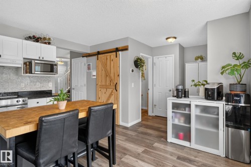 Kitchen featuring white cabinetry, stainless steel appliances, a tile backsplash, and wood-finish flooring - 833 Mcallister Crescent Sw, Edmonton, AB - Indoor Photo Showing Kitchen