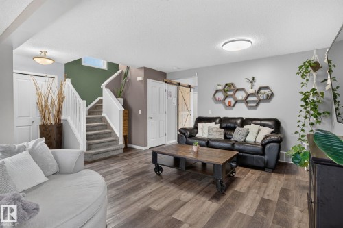 Spacious living area featuring wood-finish flooring, a carpeted staircase with white railings, and light gray wall paint - 833 Mcallister Crescent Sw, Edmonton, AB - Indoor Photo Showing Living Room