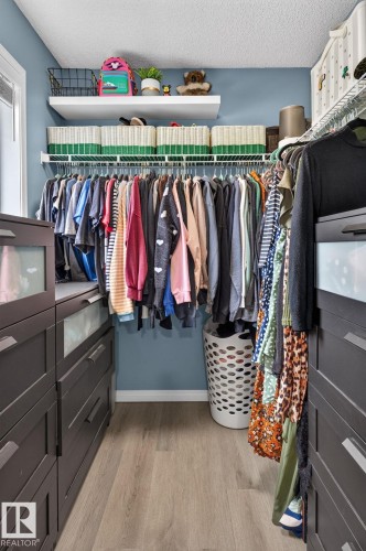 Walk-in closet featuring built-in dark wood-finish cabinetry, wire shelving, floating wall shelves, and light wood-finish flooring - 833 Mcallister Crescent Sw, Edmonton, AB - Indoor With Storage