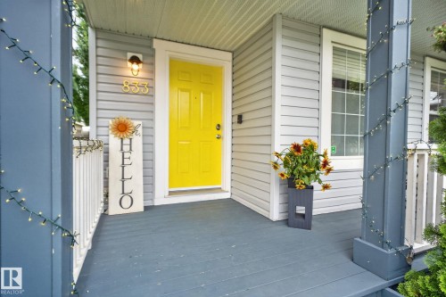 Inviting front porch featuring a vibrant yellow entry door, light gray horizontal siding, and a prominent exterior light fixture - 833 Mcallister Crescent Sw, Edmonton, AB - Outdoor With Exterior