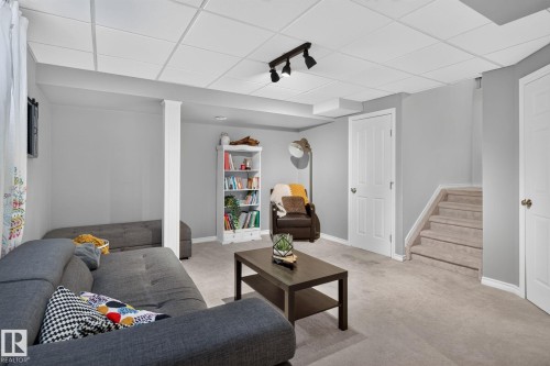 Finished lower level with neutral carpeting, recessed ceiling, track lighting, white trim, and a carpeted staircase - 833 Mcallister Crescent Sw, Edmonton, AB - Indoor Photo Showing Living Room