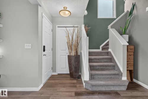 Foyer with wood-finish flooring, two-tone wall paint, and a carpeted staircase with white railings - 833 Mcallister Crescent Sw, Edmonton, AB - Indoor Photo Showing Other Room