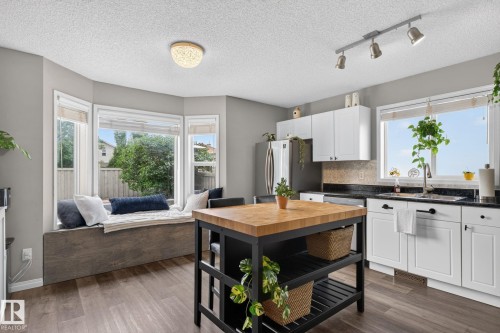 Kitchen featuring a bay window with a built-in window seat, wood-finish flooring, white cabinetry, a butcher block island, and track lighting - 833 Mcallister Crescent Sw, Edmonton, AB - Indoor Photo Showing Kitchen