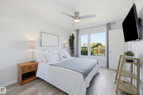 Bedroom featuring light wood-finish flooring, a contemporary ceiling fan with integrated lighting, a large window, and a wall-mounted flat-screen television - 15111 67 Street Nw, Edmonton, AB - Indoor Photo Showing Bedroom
