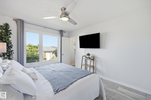 Bright interior with a large double-pane window, flush-mount ceiling fan, wall-mounted television, and wood-finish flooring - 15111 67 Street Nw, Edmonton, AB - Indoor Photo Showing Bedroom