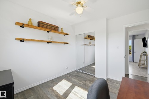 Room featuring wood-finish flooring, two natural wood floating shelves with black brackets, and a ceiling fan with integrated lighting - 15111 67 Street Nw, Edmonton, AB - Indoor