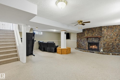 Carpeted basement recreation room featuring a stone-faced fireplace with a wood mantle, a ceiling fan, and recessed lighting - 15111 67 Street Nw, Edmonton, AB - Indoor With Fireplace
