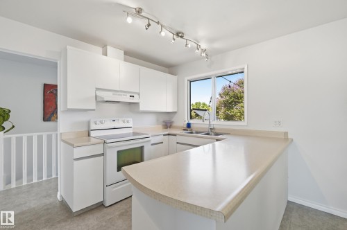 Modern kitchen featuring white cabinetry, a white electric range, and light-toned countertops - 15111 67 Street Nw, Edmonton, AB - Indoor Photo Showing Kitchen With Double Sink