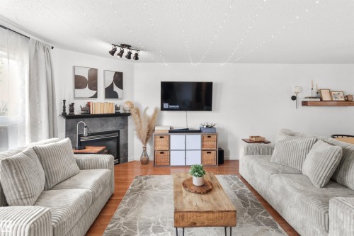 Spacious living area featuring warm wood-finish flooring, a contemporary fireplace with a dark stone surround, and a track lighting fixture - 679 Kananaskis Drive, Devon, AB - Indoor Photo Showing Living Room With Fireplace
