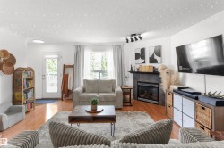 Living area with wood-finish flooring, a corner fireplace featuring dark tile surround and a mantel, and a door offering exterior access - 