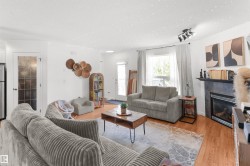Bright living area featuring wood-finish flooring and a corner fireplace with a dark stone surround - 