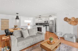 Open-concept living space featuring wood-finish flooring, white walls, and a modern kitchen with stainless steel appliances - 