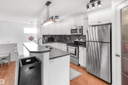 Kitchen featuring white shaker-style cabinetry, stainless steel appliances, a dark countertop, a diamond-patterned backsplash, and wood-finish flooring - 