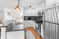 Kitchen featuring white cabinetry, stainless steel appliances, dark countertops, a dual basin sink, and wood-finish flooring - 