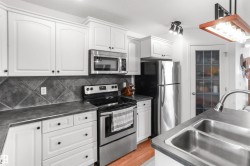 Bright kitchen featuring white cabinetry, stainless steel appliances, dark tile backsplash, and a double basin sink with a gooseneck faucet - 