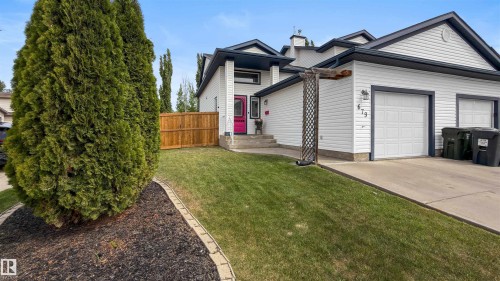 White siding exterior with dark trim accents and a vibrant red entry door - 679 Kananaskis Drive, Devon, AB - Outdoor