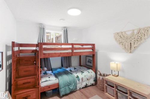 Bedroom featuring wood-finish flooring, a bright window with light-filtering curtains, and a flush-mount ceiling light - 679 Kananaskis Drive, Devon, AB - Indoor Photo Showing Bedroom